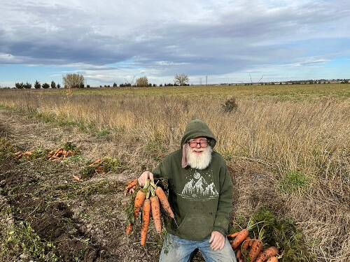 Meadowlark Hearth owner in a field holding up carrots